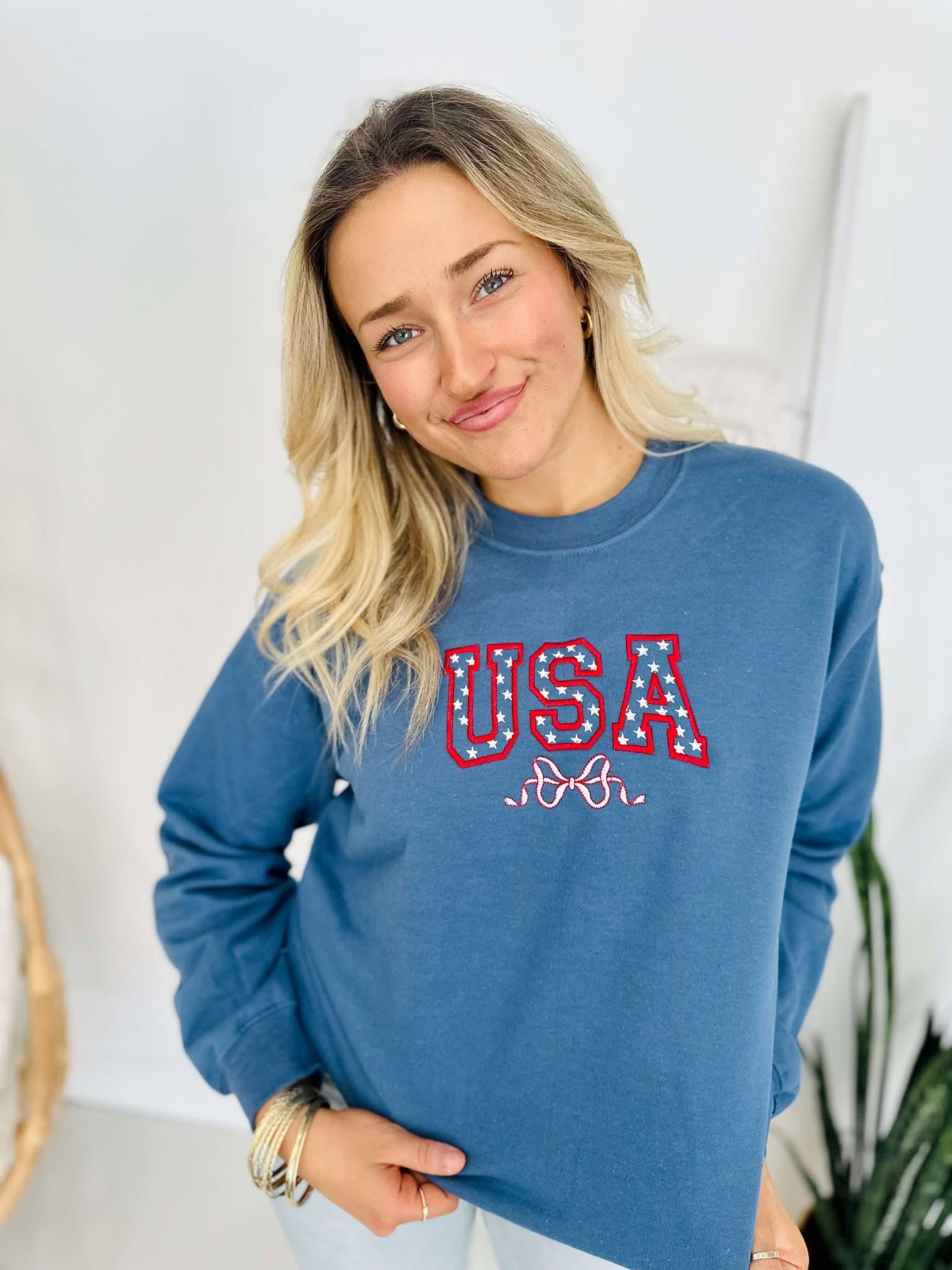 A woman wearing a blue sweatshirt with 'USA' and a star and bow embroidered on the front.