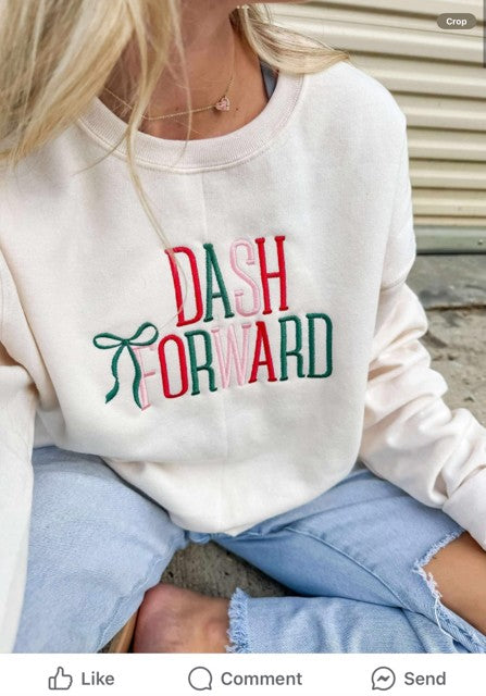Person wearing a sweet cream sweatshirt with 'DASH FORWARD' text and a green bow embroidery in Christmas colors