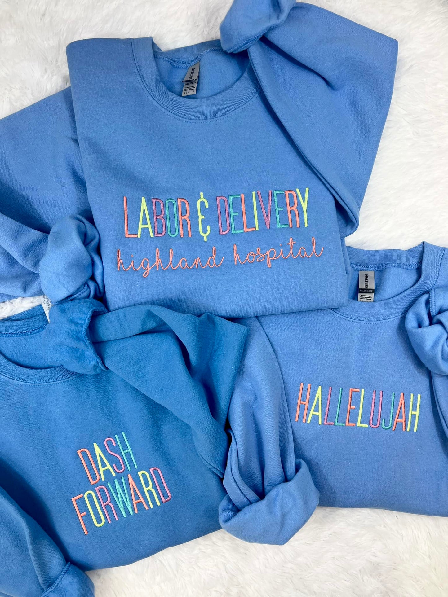 A collection of blue sweatshirts with custom embroidered text on them, like Dash Forward, displayed on a white background.