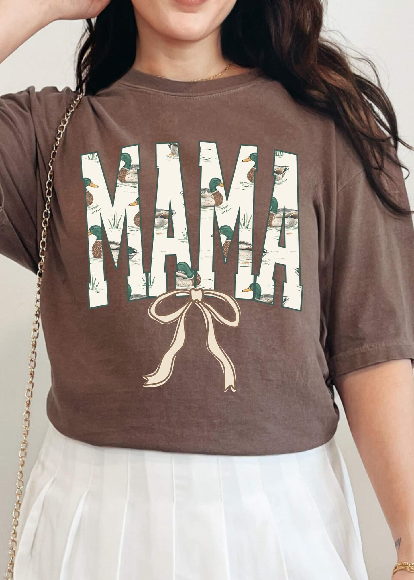 A person wearing a brown DTF tee with the word 'MAMA' and a graphic of ducks and a bow on it.