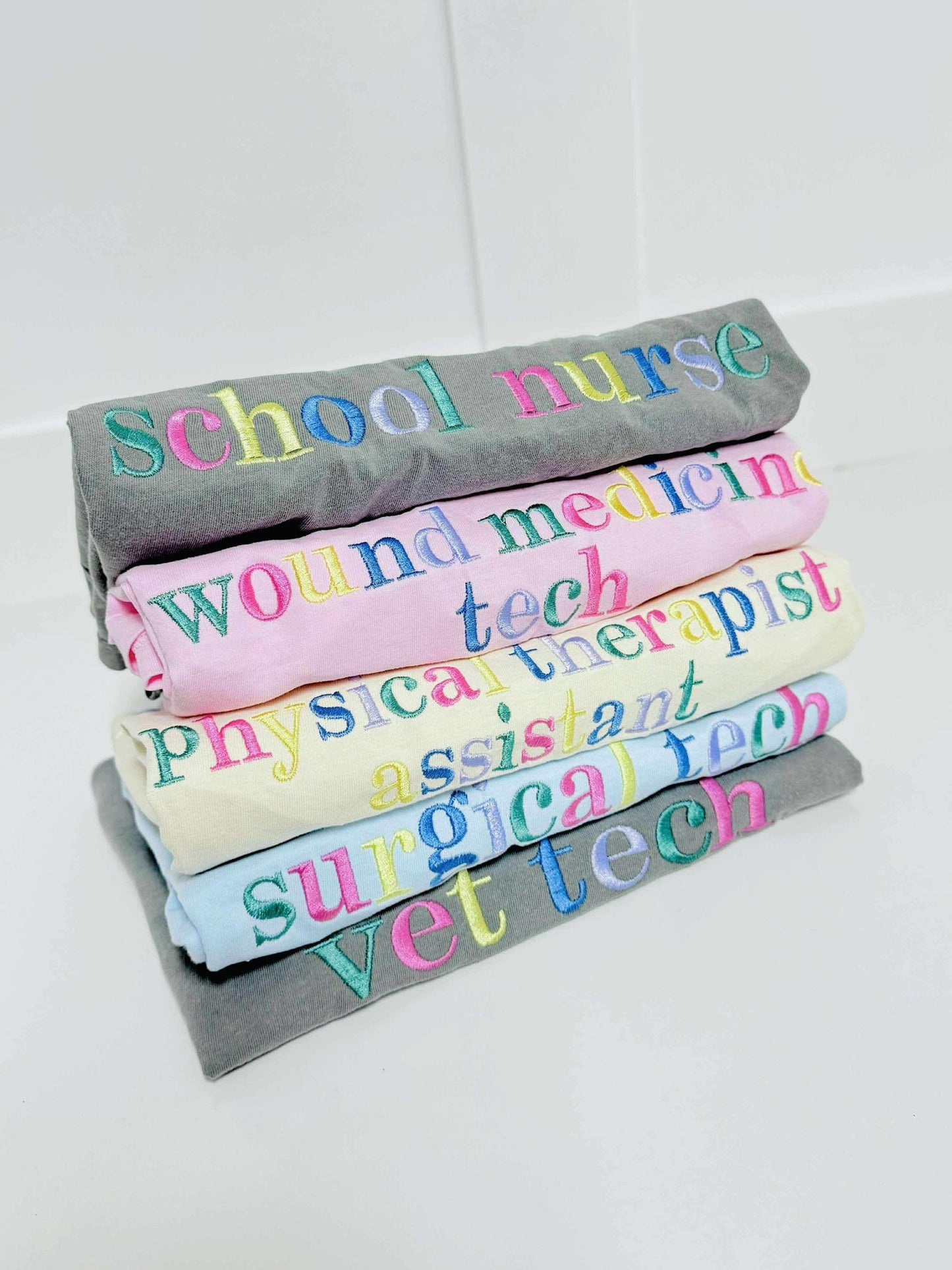 Stack of rolled-up shirts with colorful embroidery shop names on a white background