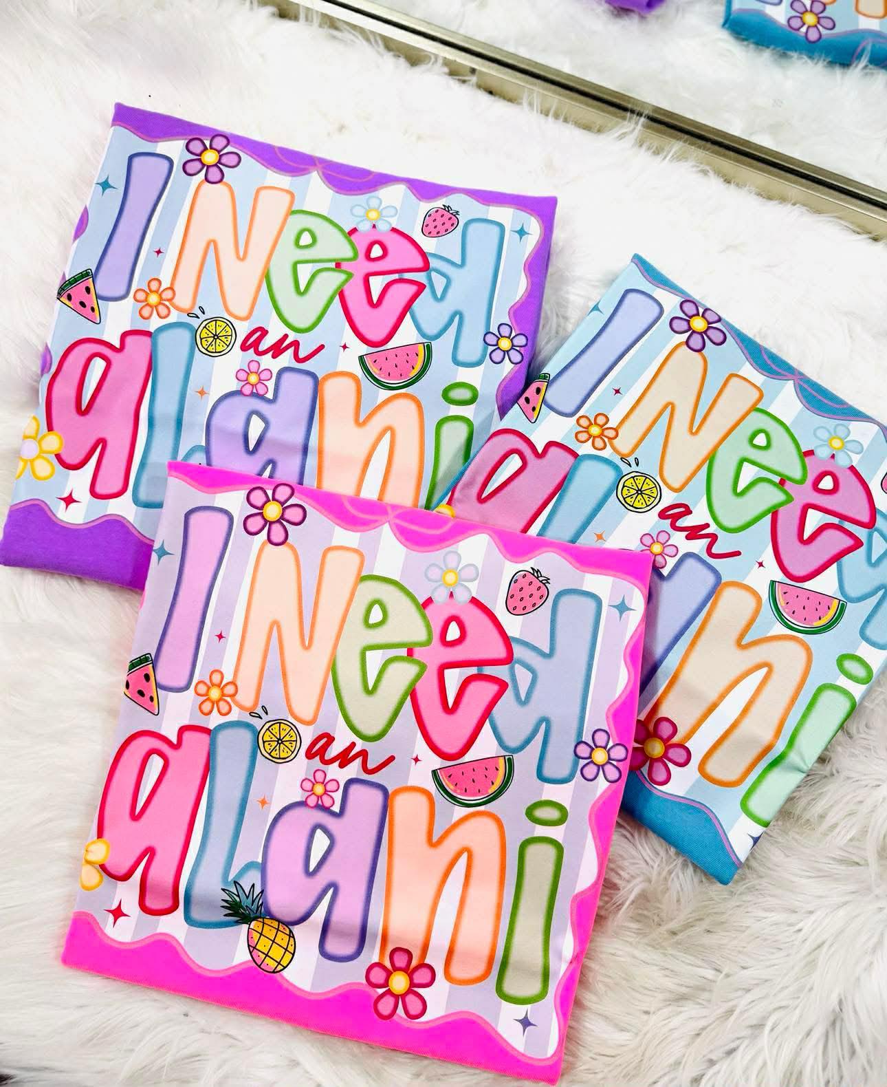 Colorful neon tee shirts with 'I need a alani' multi color dtf on a white surface