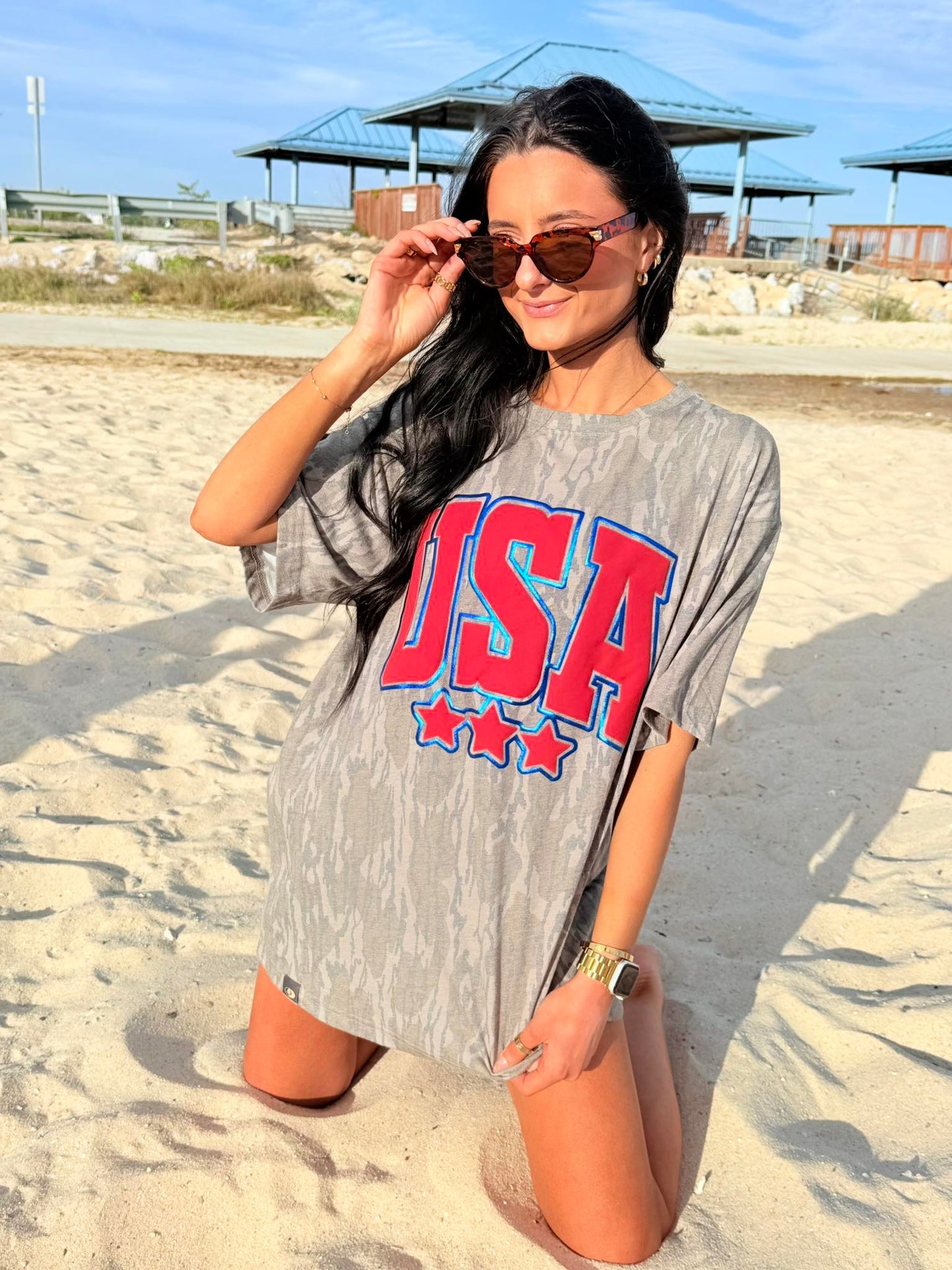 Woman wearing a bottomland 'USA' t-shirt on a sandy beach.