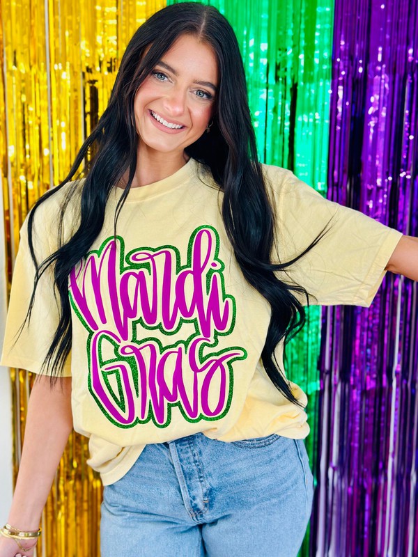 A person wearing a yellow t-shirt with neon purple and green glitter, and the text 'MARDI GRAS' in cursive script.