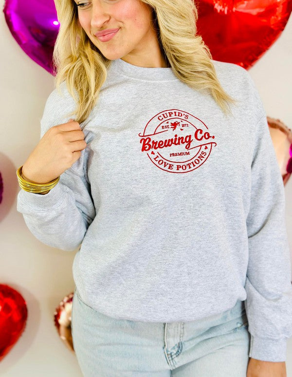 Person wearing a gray sweatshirt with 'Cupid Brewing Co.' logo, surrounded by heart-shaped balloons.
