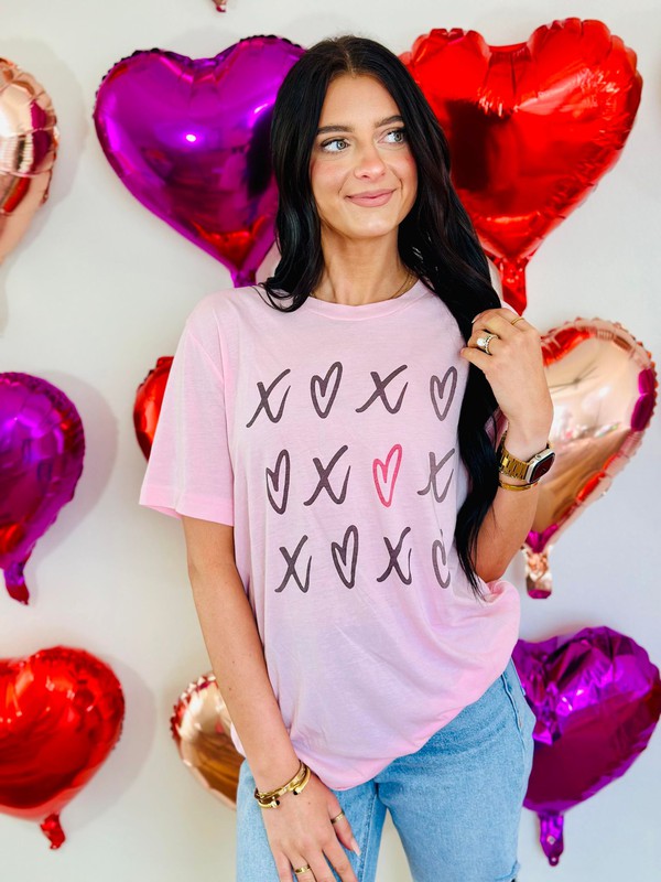 A person wearing a pink t-shirt with heart and 'XOXO' text design, surrounded by balloons and decorations with a Valentine's Day theme.