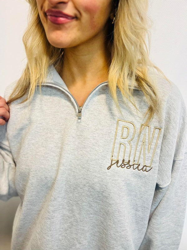 A woman wearing a gray sweatshirt with 'RN' embroidered on the front.