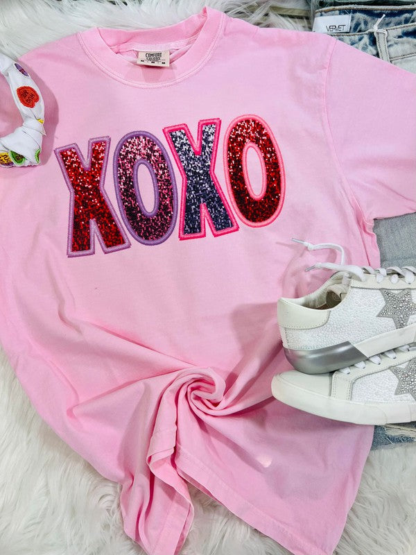 Pink sweatshirt with 'XOXO' in colorful letters on a white surface.