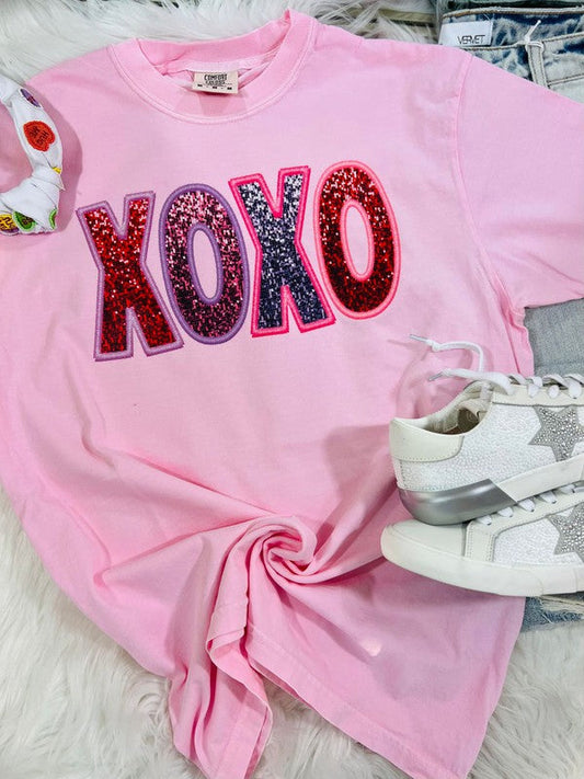 Pink sweatshirt with 'XOXO' in colorful letters on a white surface.