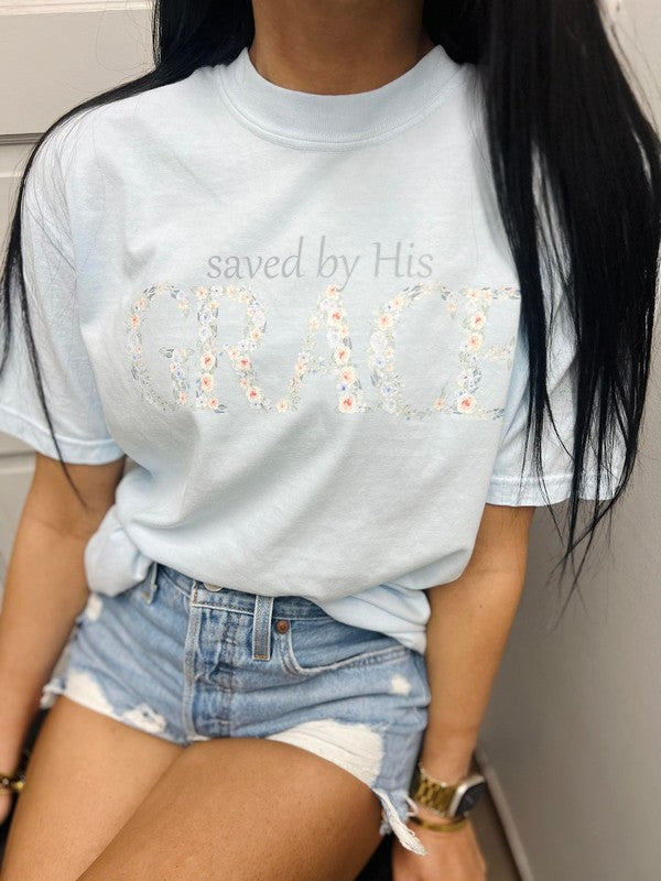 A person wearing a light blue t-shirt with the text 'saved by His grace' and a floral design.