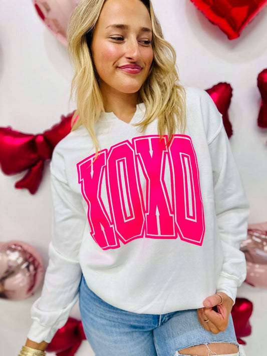 A person wearing a white V-neck sweatshirt with 'XOXO' printed in neon pink vinyl on the front.
