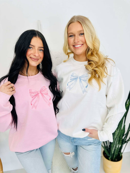 Two individuals standing next to each other, one wearing a pink and the other wearing a white embroidered bow sweatshirt.