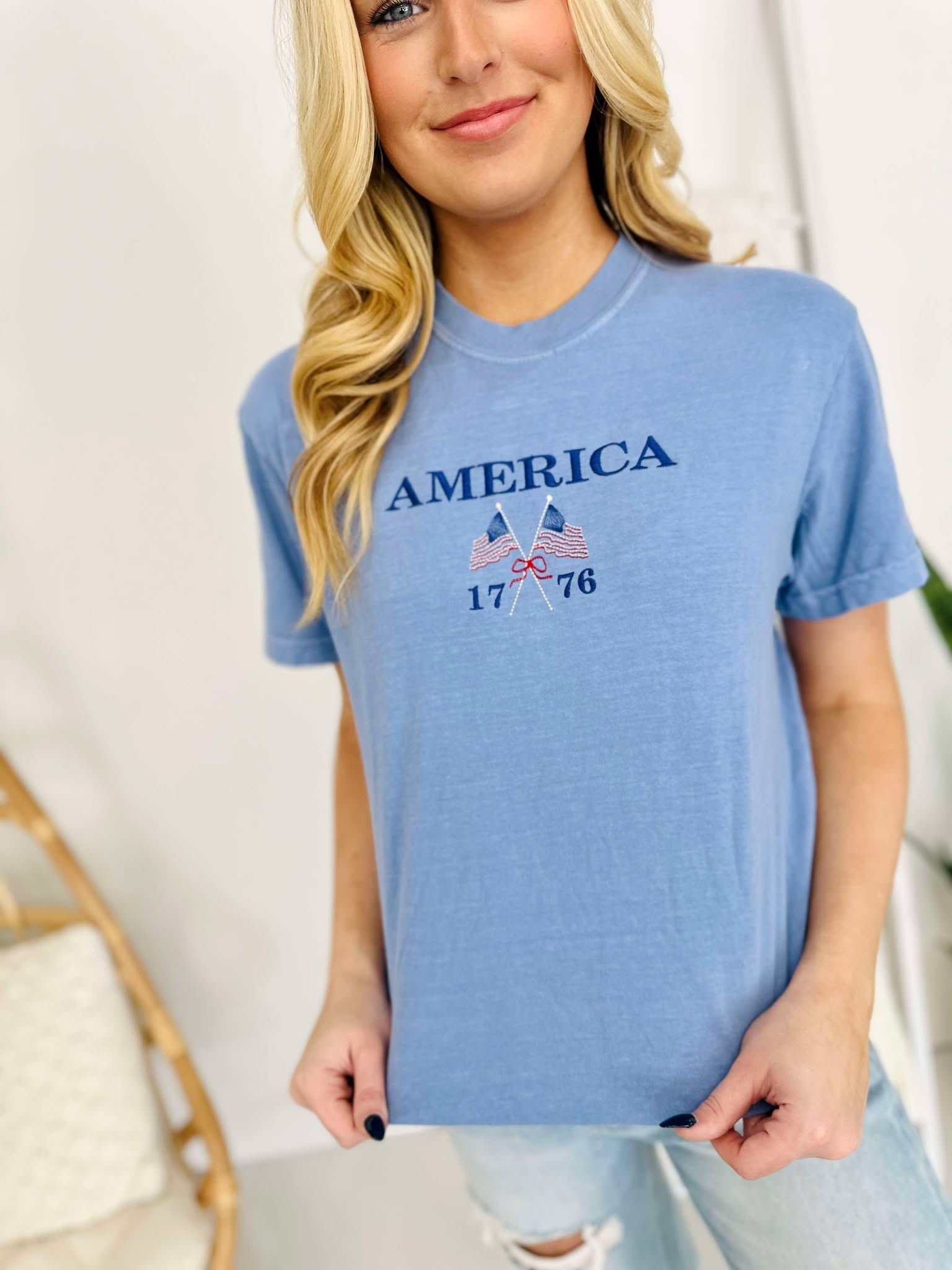 A woman wearing a blue t-shirt with 'America 1776' and a flag-themed design embroidered on the front.