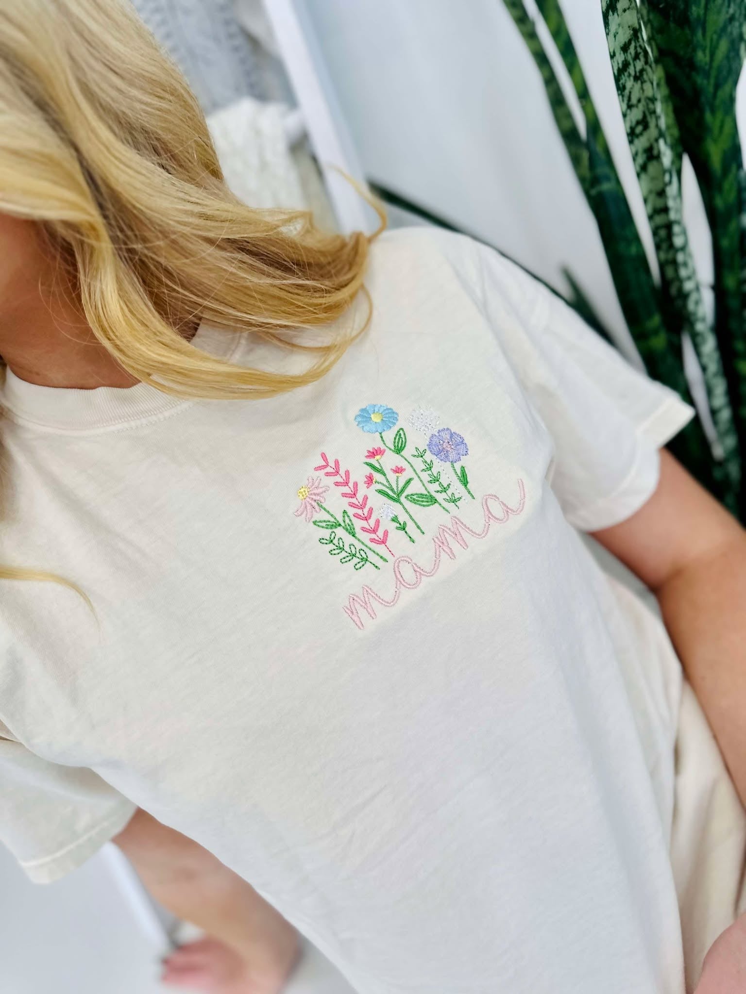 A woman wearing a white short-sleeved t-shirt with embroidered floral design and the word 'mama' on the front.