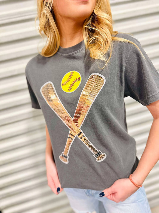 A female model wearing a gray t-shirt with a sequin patch on the front showing two softball bats and a yellow softball.