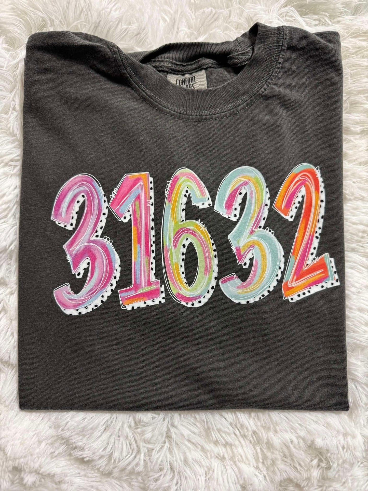 A folded black t-shirt with the zip code '31632' painted in various colors on the front.