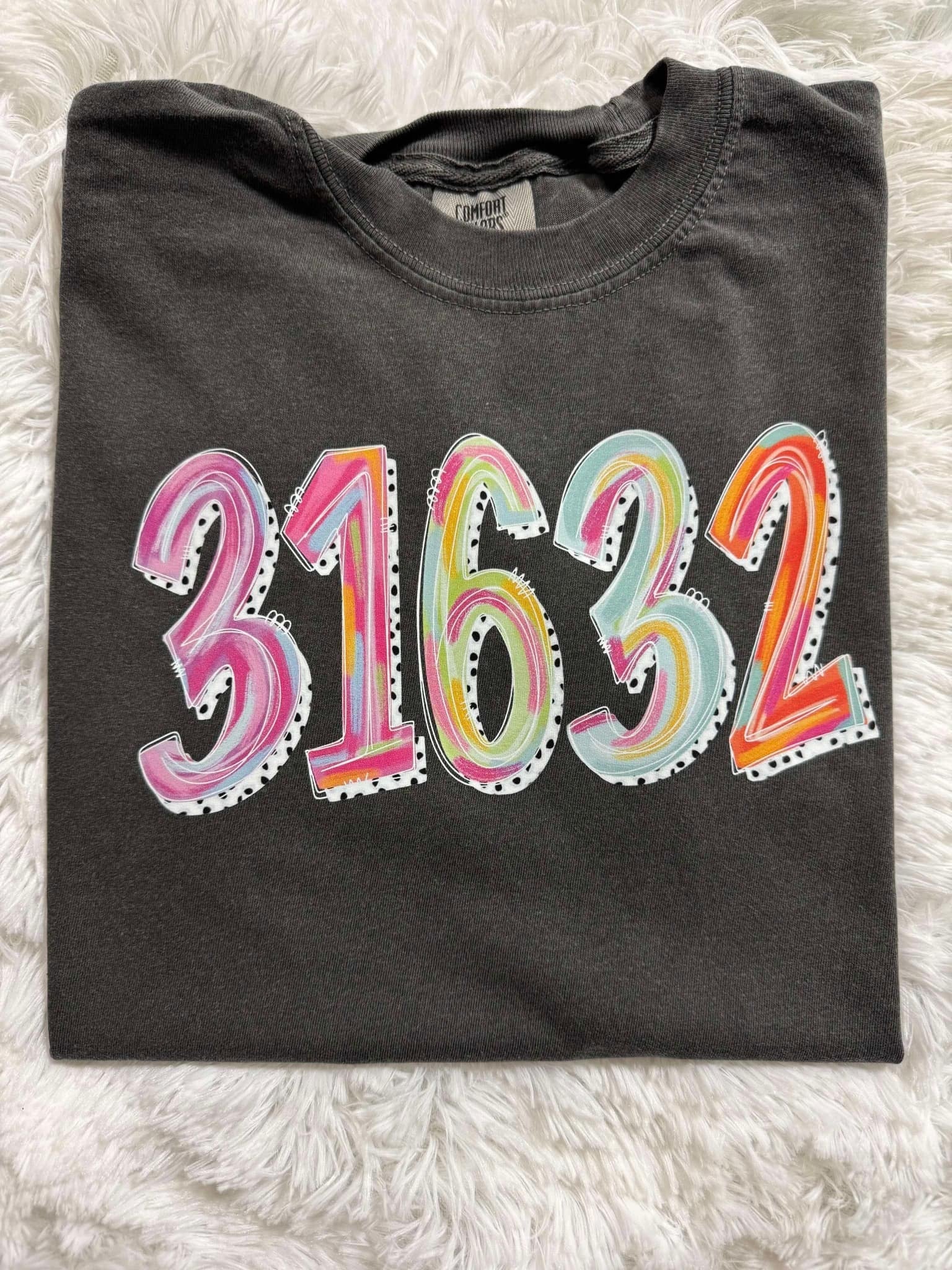 A folded black t-shirt with the zip code '31632' painted in various colors on the front.