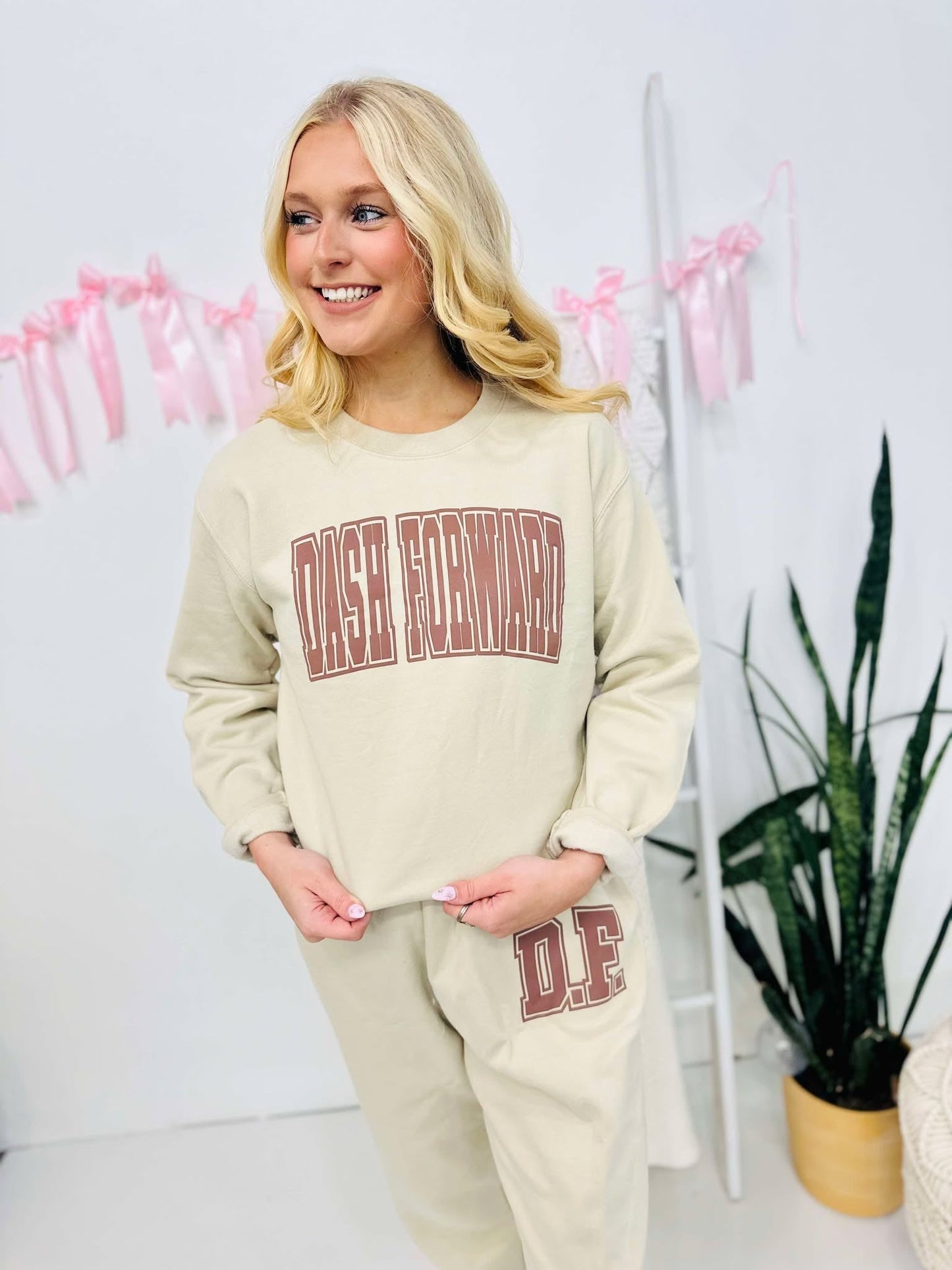 A person wearing a Tan sweatshirt and matching sweatpants set with brown puff text vinyl puff graphics.