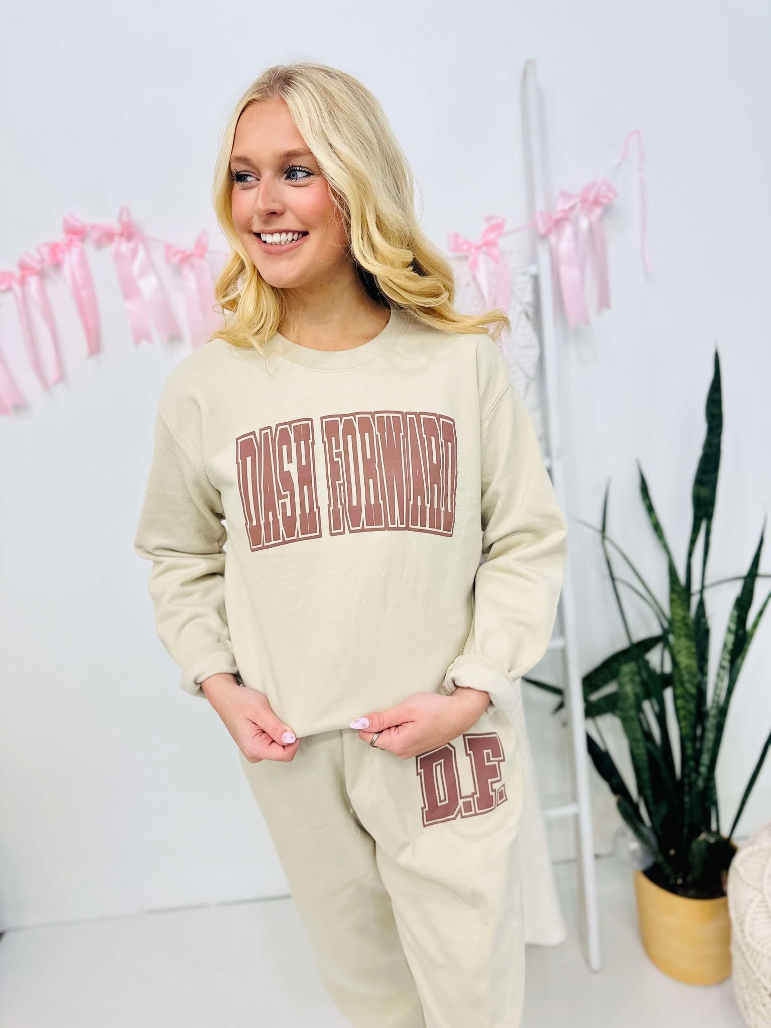 A person wearing a Tan sweatshirt and matching sweatpants set with brown puff text vinyl puff graphics.