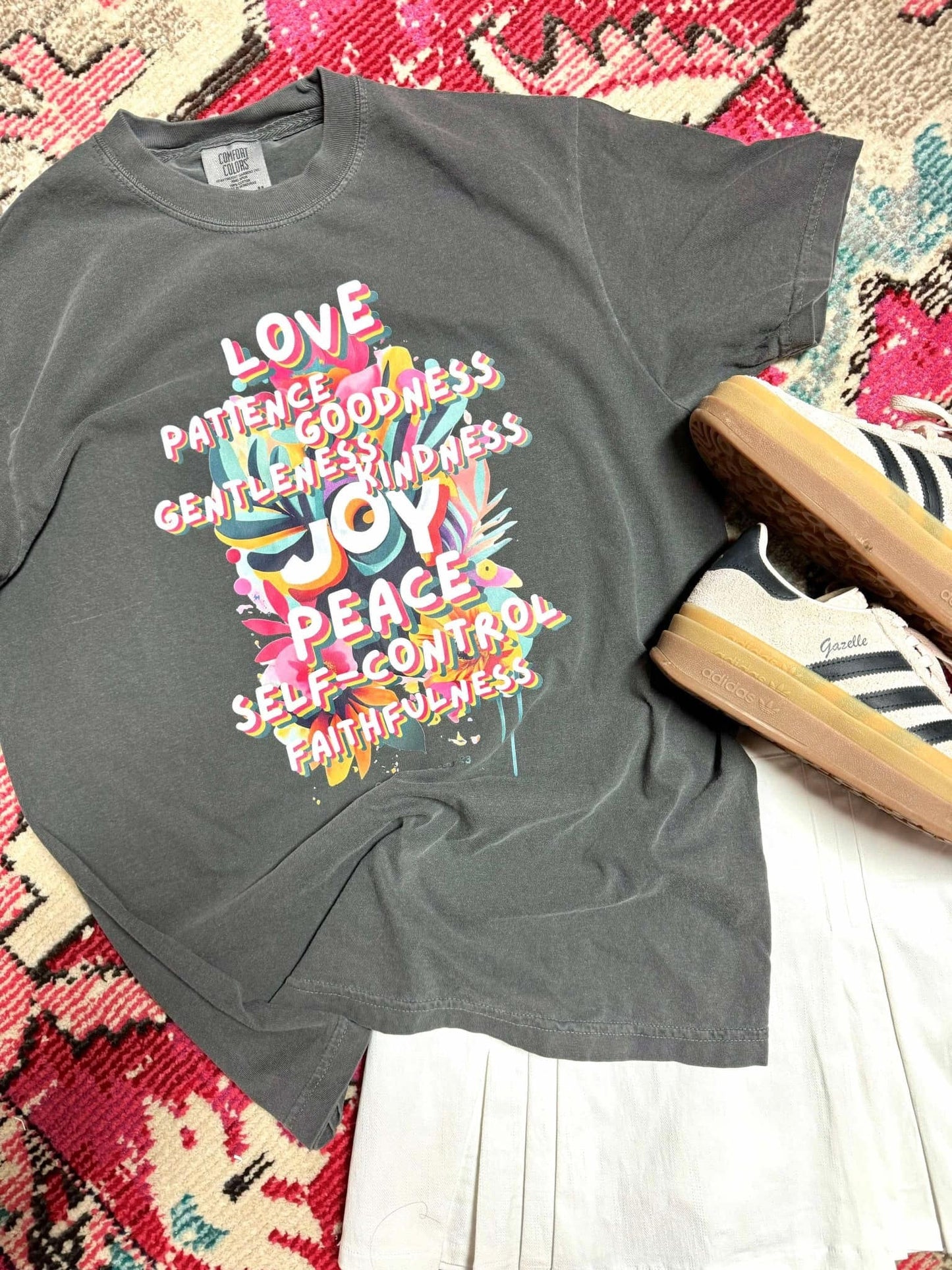 A gray t-shirt laid out on a patterned surface, featuring a printed design with the fruits of the spirit, accompanied by a pair of shoes.