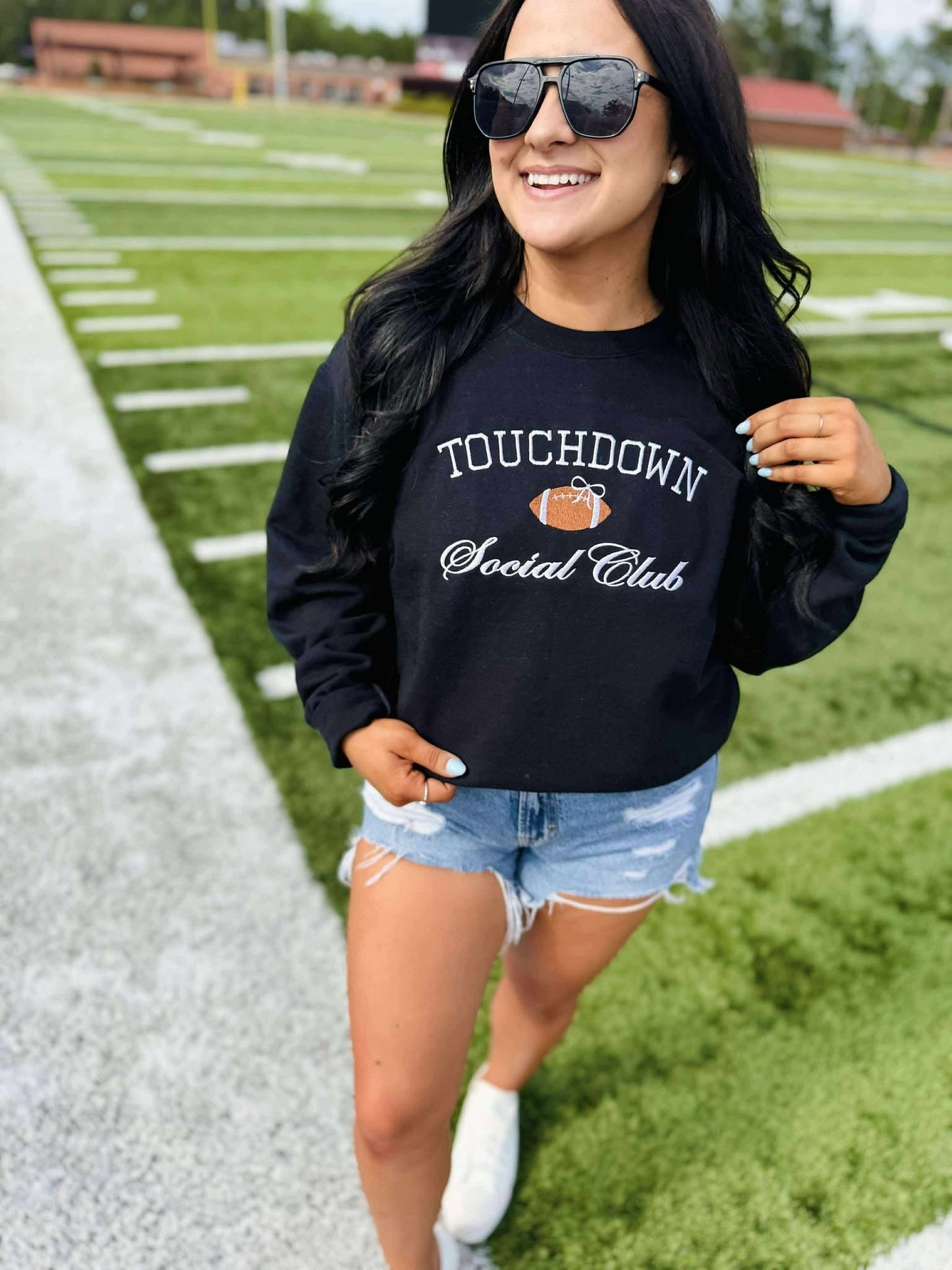 Woman wearing a black sweatshirt with 'Touchdown Social Club' text on a grassy field.