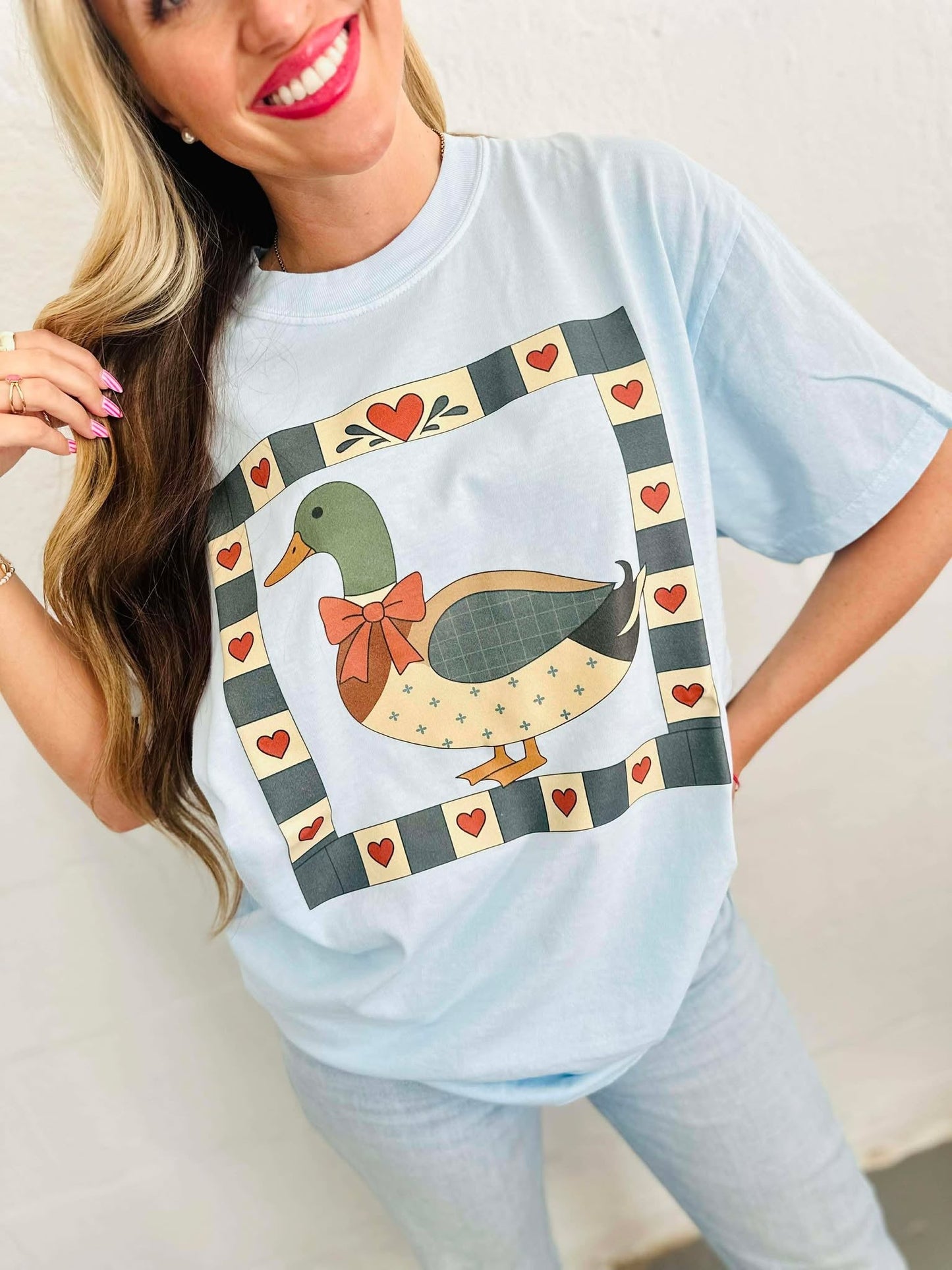 Woman wearing a light blue t-shirt with a duck mallard patchwork graphic design.
