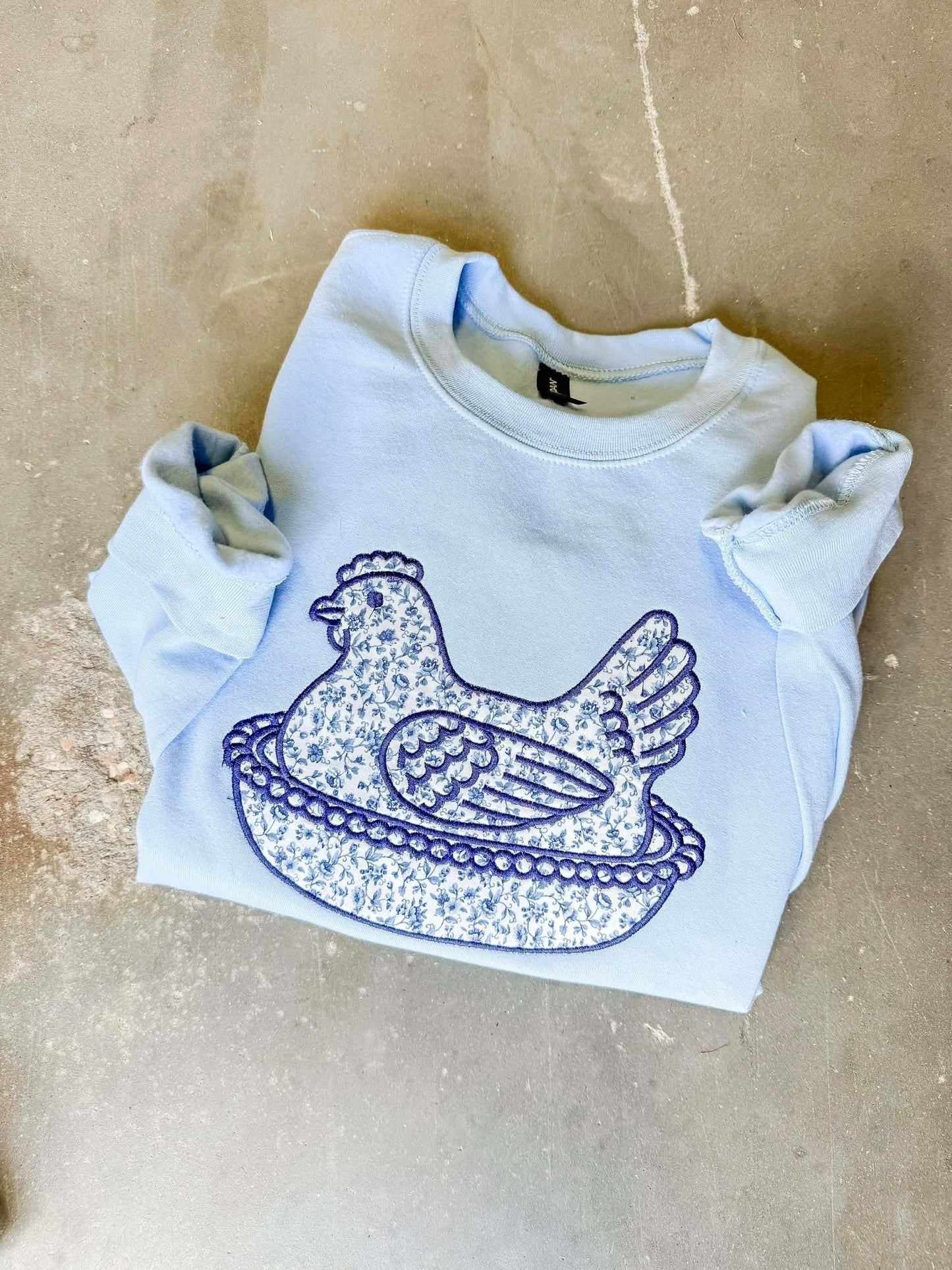 White sweatshirt with blue graphic design on a beige surface