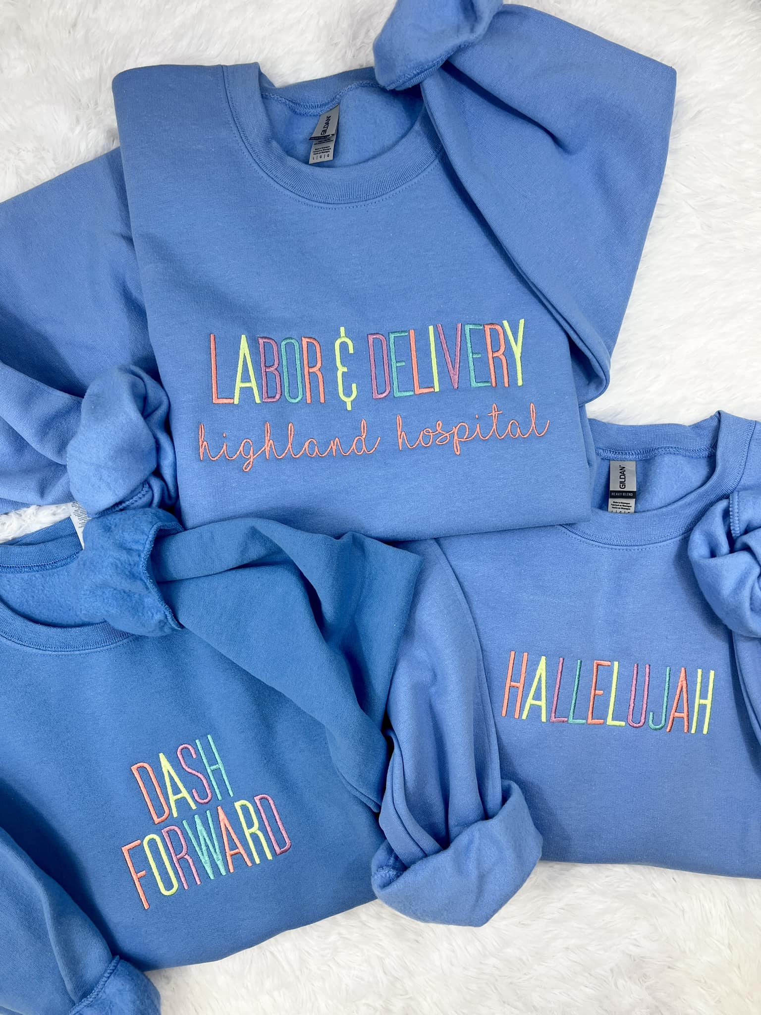 A collection of blue sweatshirts with custom embroidered text on them, like Dash Forward, displayed on a white background.