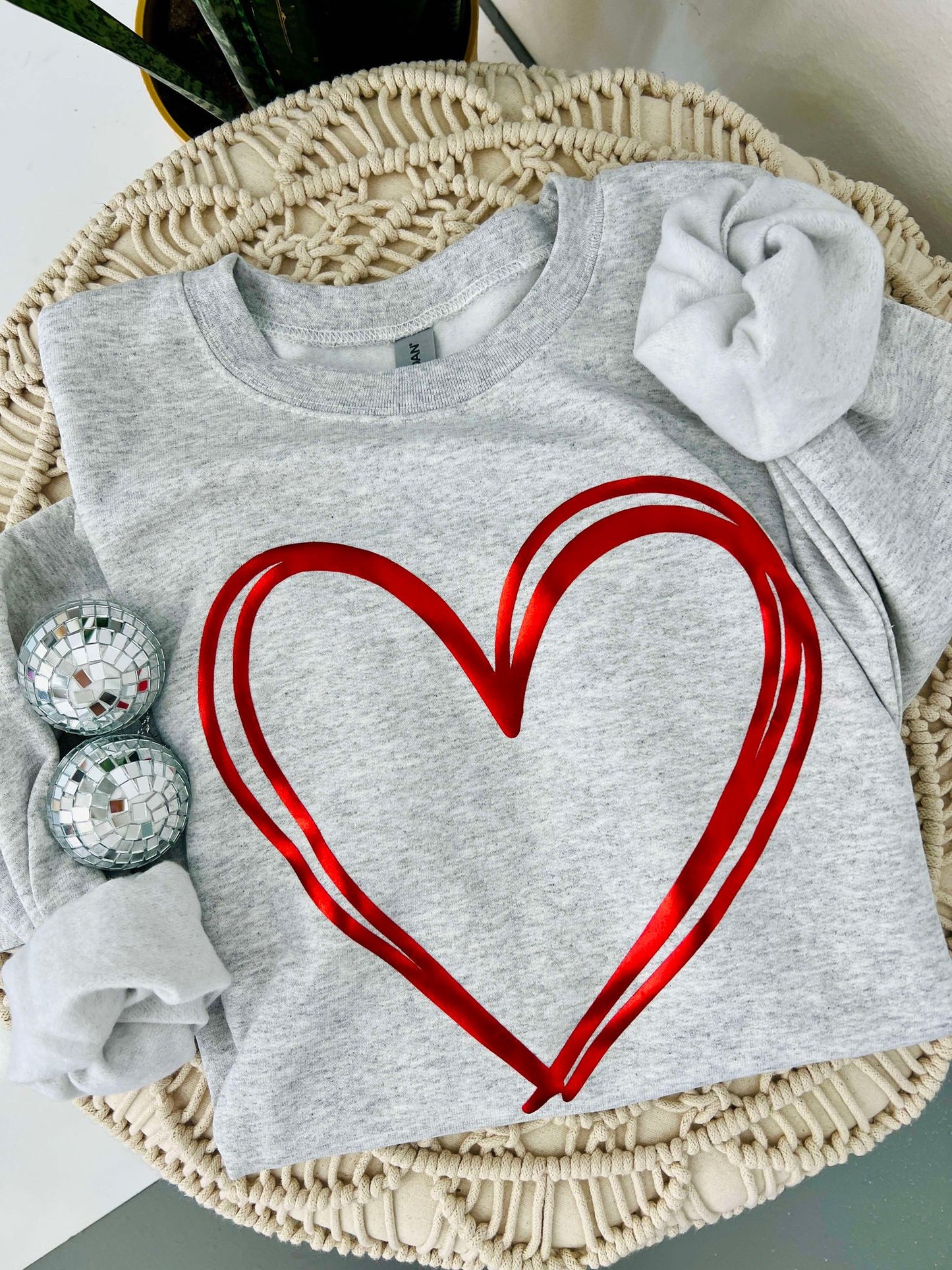 A gray sweatshirt with a red metallic puff vinyl heart design, displayed on a mannequin set in a home decor environment.