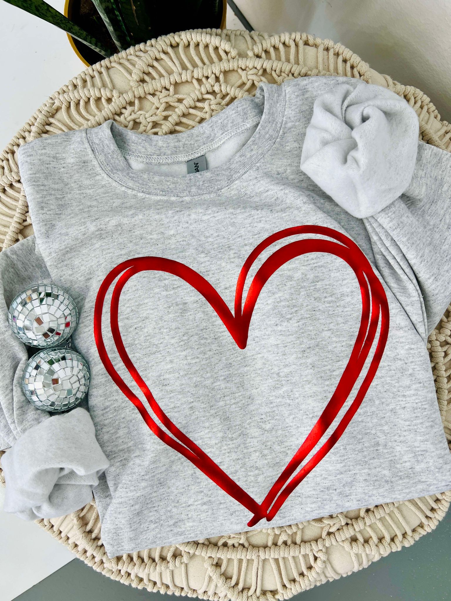 A gray sweatshirt with a red metallic puff vinyl heart design, displayed on a mannequin set in a home decor environment.
