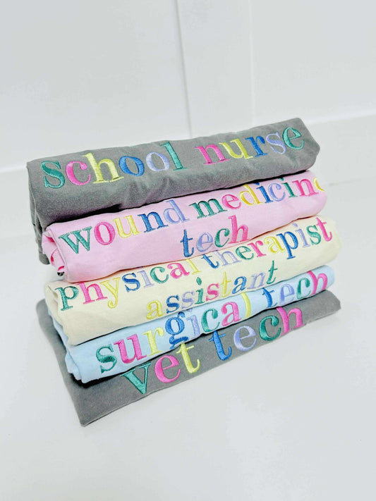Stack of rolled-up shirts with colorful embroidery shop names on a white background