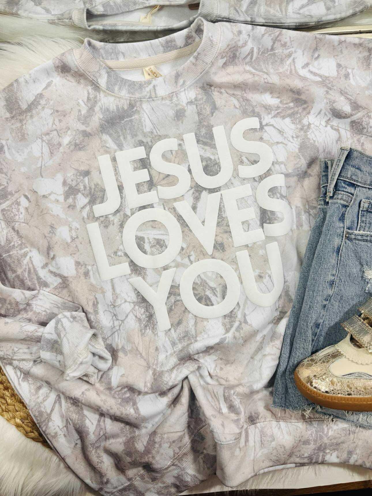 T-shirt with 'Jesus Loves You' text on a marble surface with jeans and shoes.