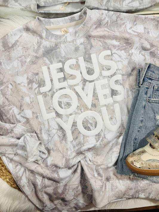 T-shirt with 'Jesus Loves You' text on a marble surface with jeans and shoes.