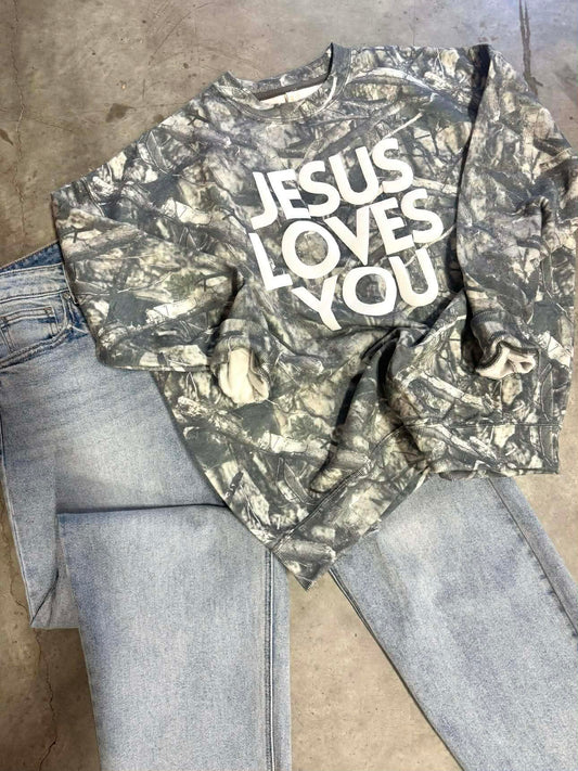 Camouflage long-sleeve shirt with 'Jesus Loves You' text on a concrete floor.