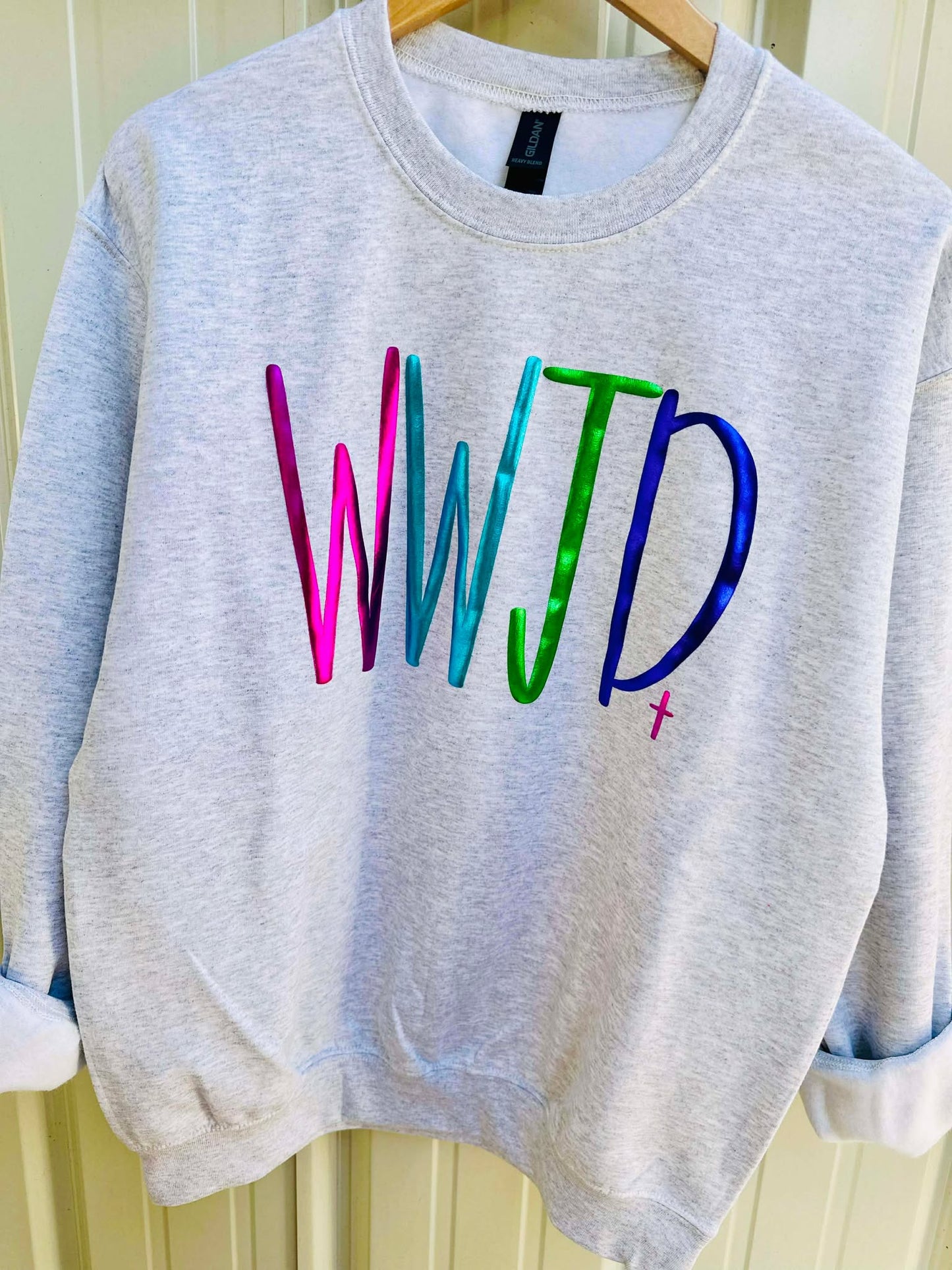 Gray sweatshirt with colorful 'WWJD' text on a hanger against a white wall.