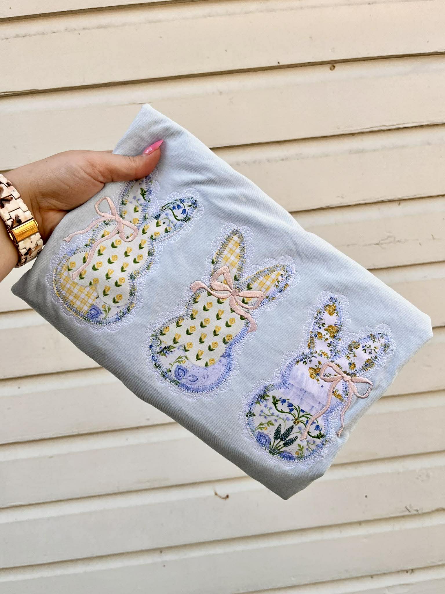 Hand holding a folded embroidered tee with lace bunny designs against a wooden background
