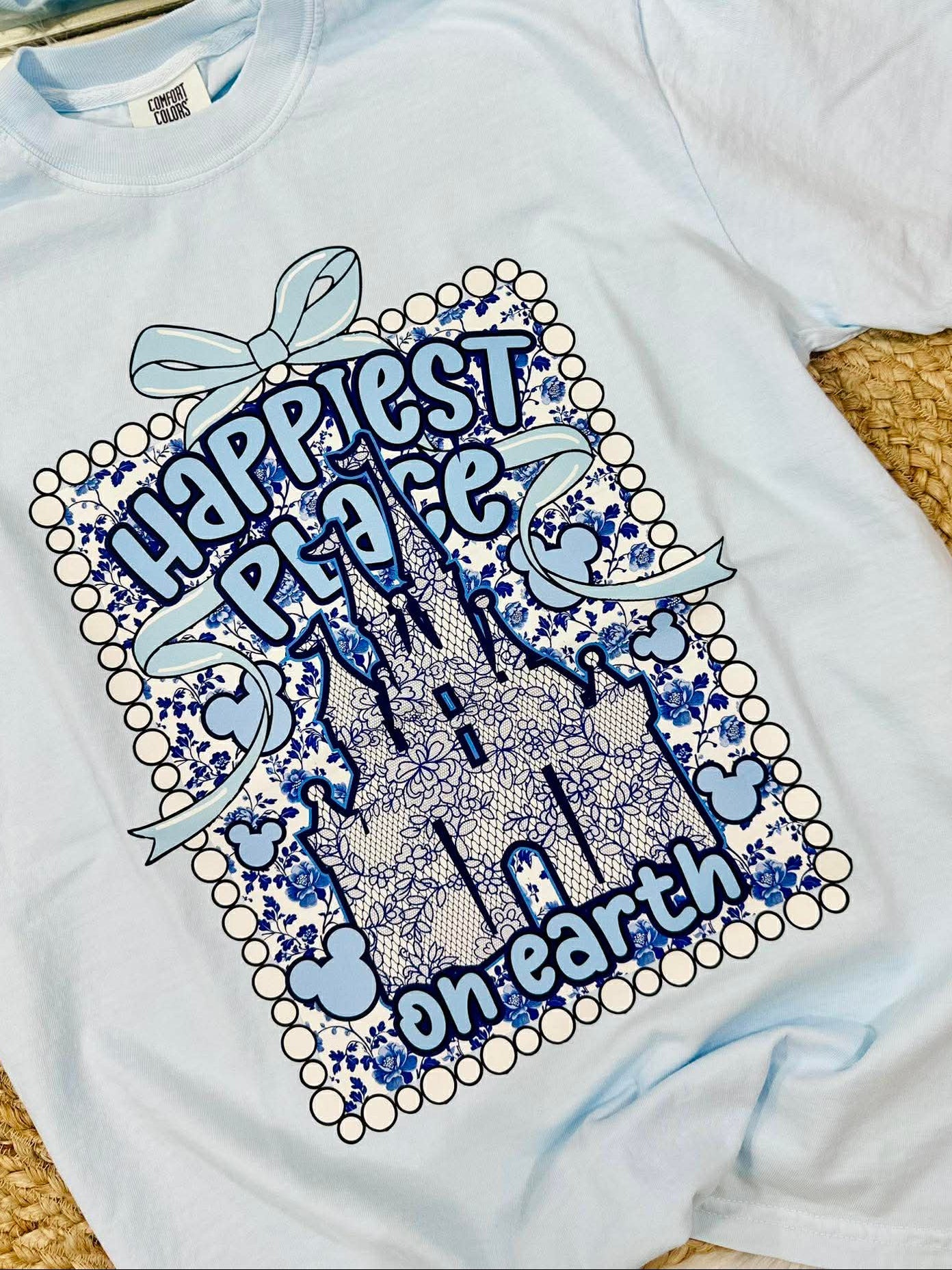 White t-shirt with blue castle design and text 'Happiest Place on Earth' on a textured surface.