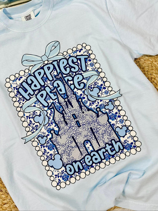 White t-shirt with blue castle design and text 'Happiest Place on Earth' on a textured surface.