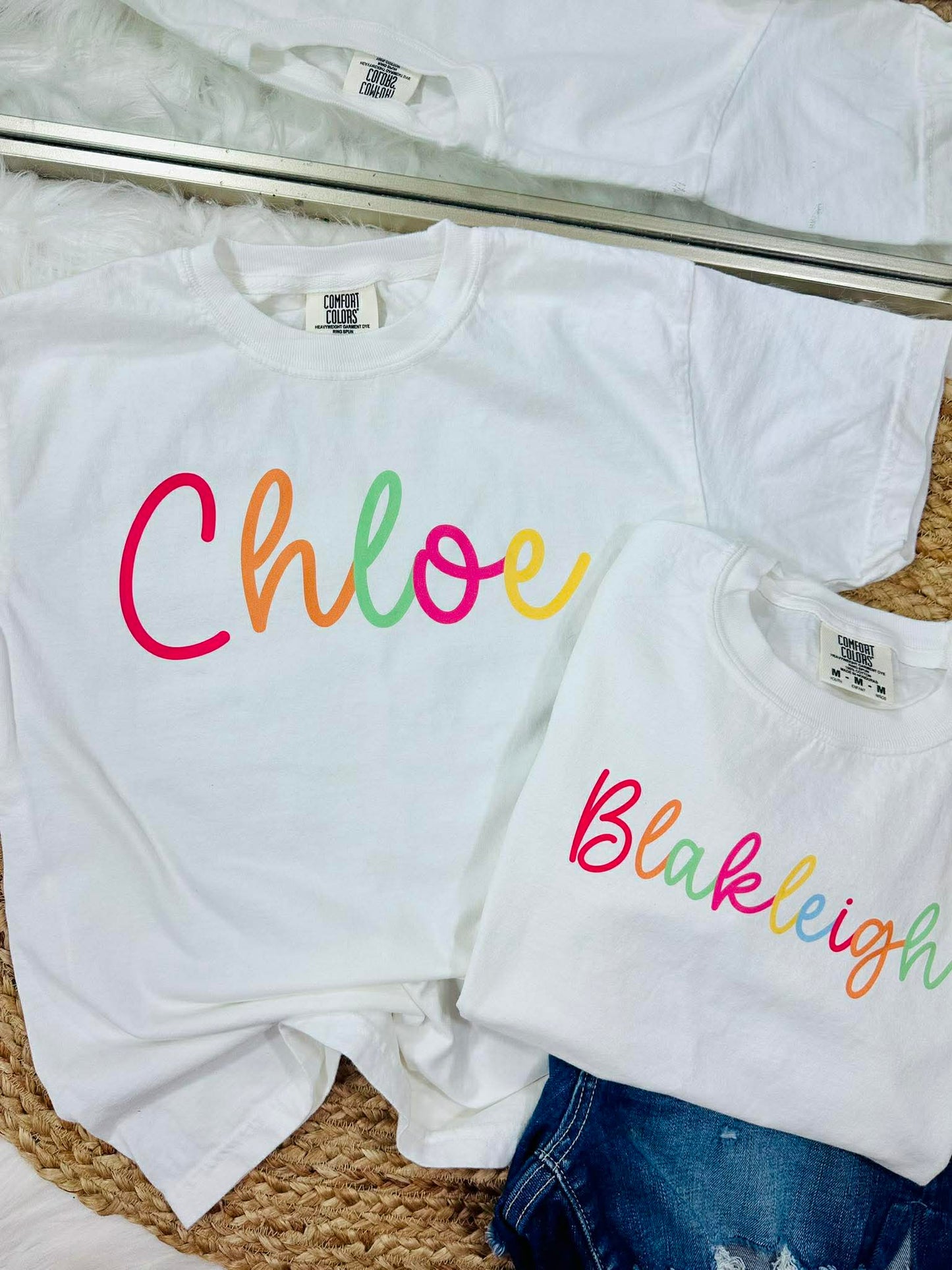 White t-shirts with colorful names 'Chloe' and 'Blakleigh' on a textured surface.