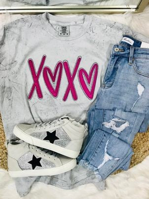 A Smoke Comfort Color t-shirt with pink 'XOXO' heart applique, paired with blue denim jeans and white sneakers with a star pattern.