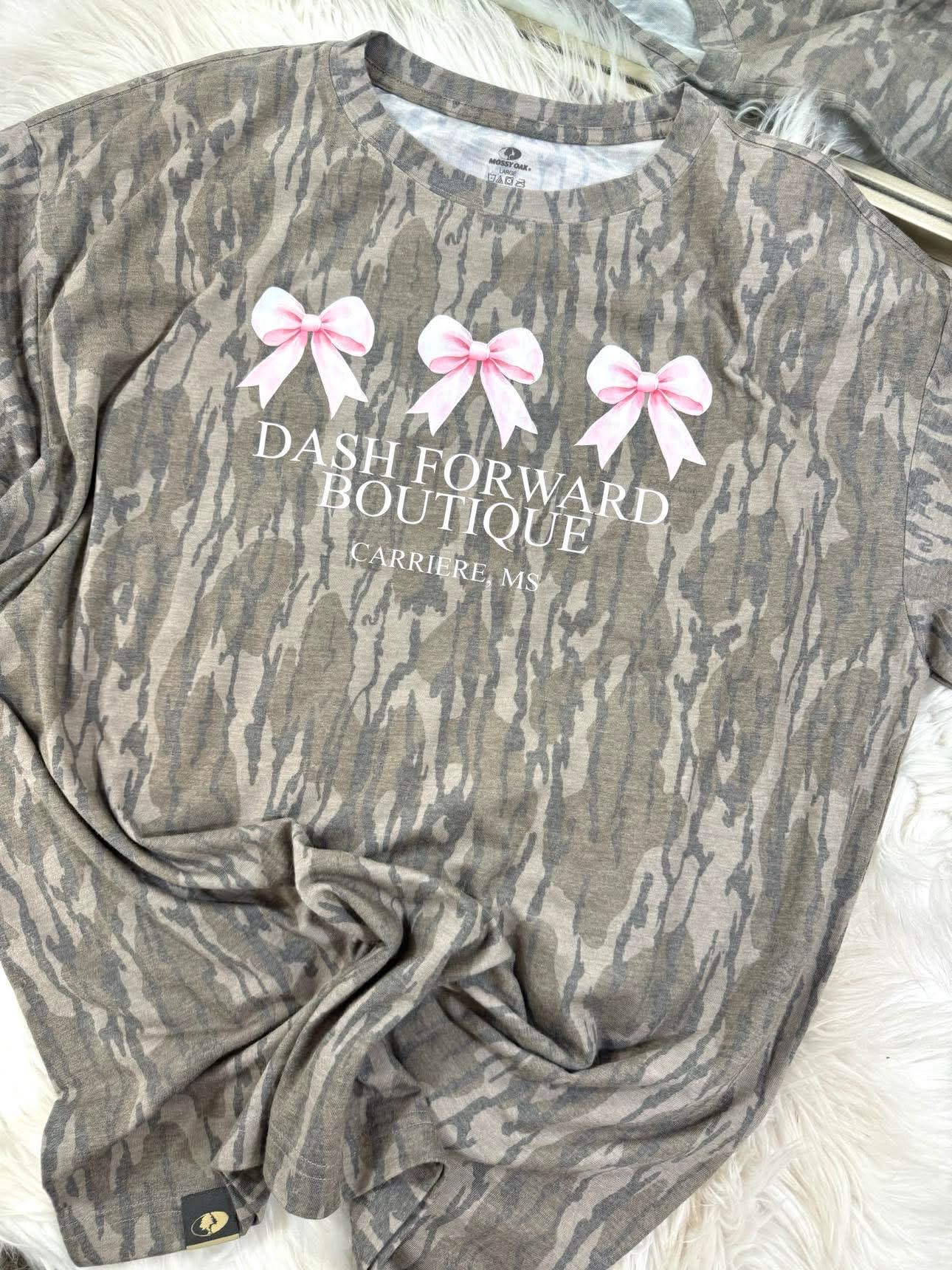Mossy Oak Camouflage shirt with 'Dash Forward Boutique' text and pink bows on a white surface