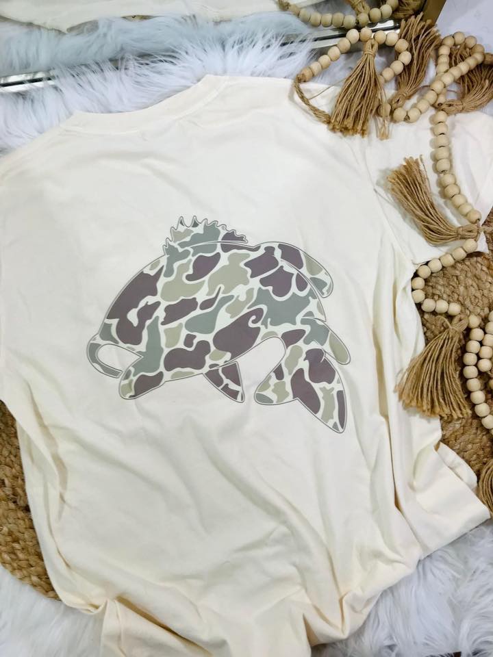 Ivory tee with a camouflage fish design on a rug surface.