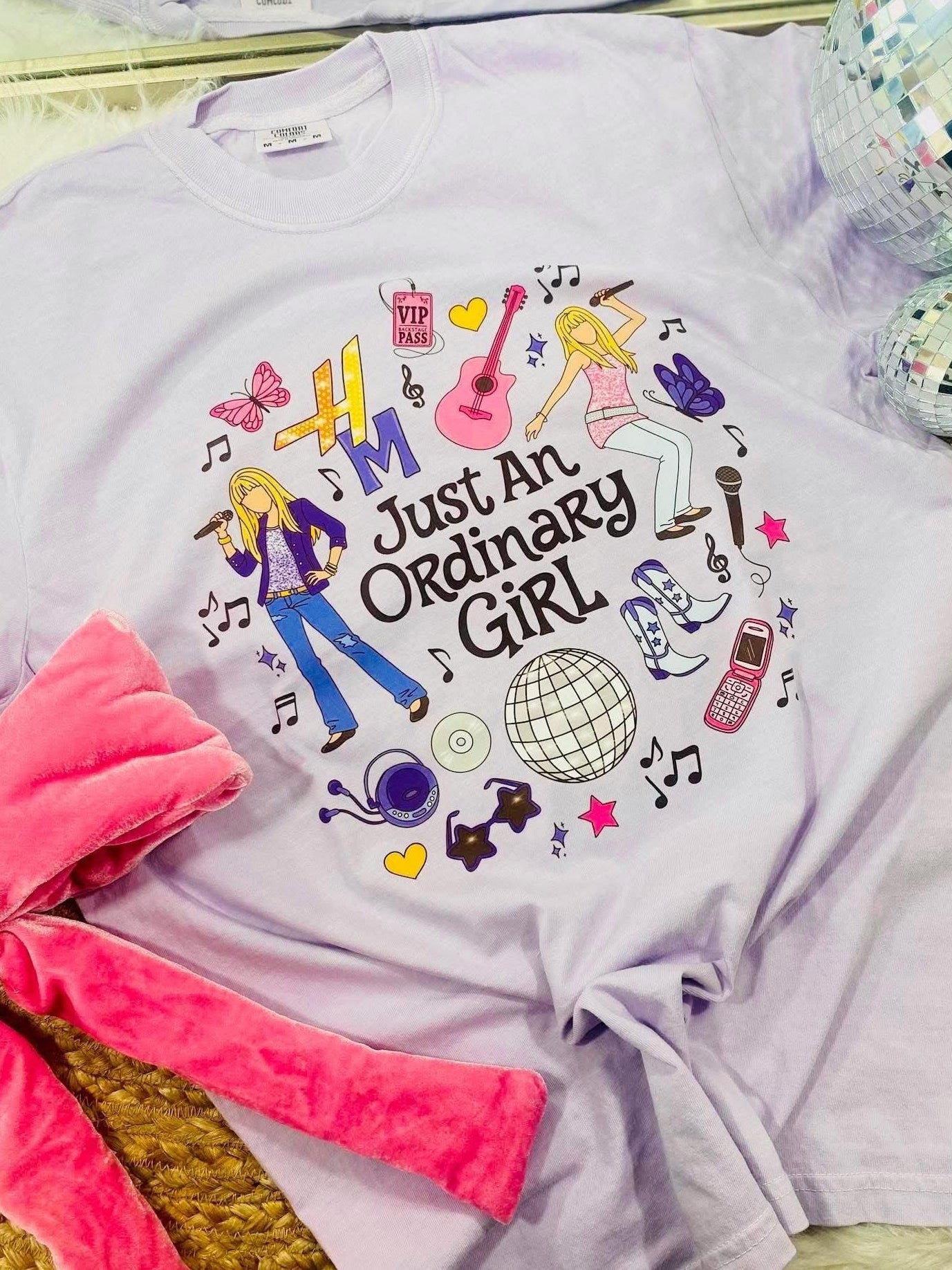 White t-shirt with colorful graphic design and text 'Just An Ordinary Girl' on a reflective surface.